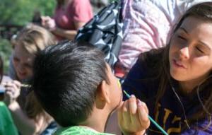 A Communication Sciences student paints a child's face at an event.